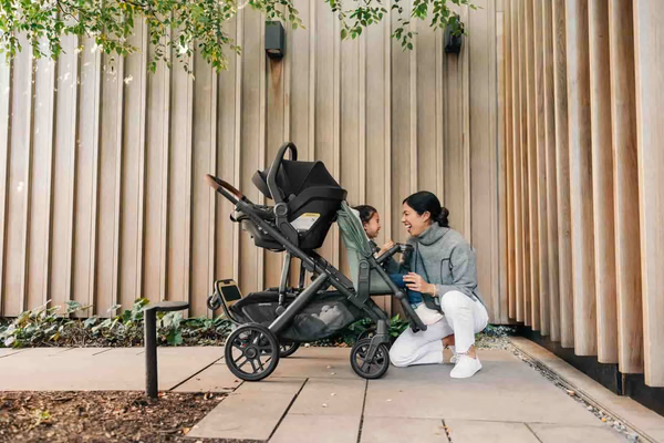 A mom crouching beside a convertible stroller with an infant car seat attached